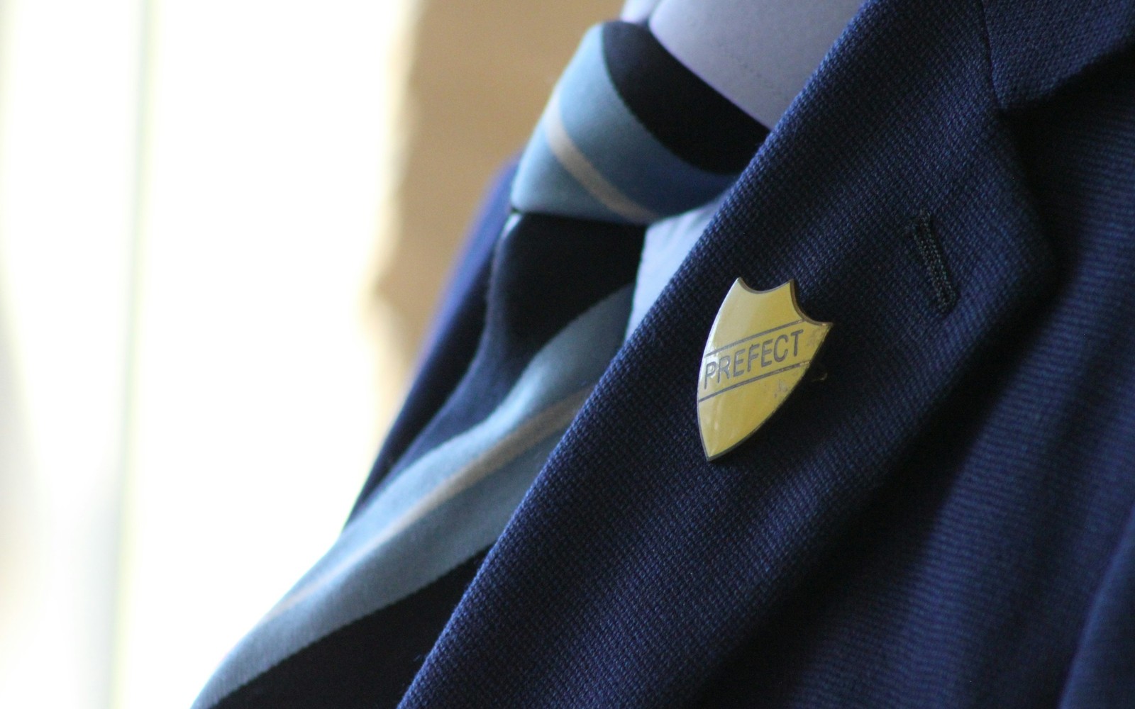 A UK school blazer with a prefect badge and tie